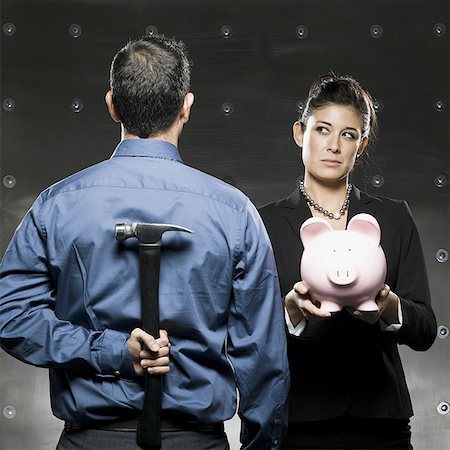 woman holding a piggy bank and a man holding a hammer behind his back Stock Photo - Premium Royalty-Free, Code: 640-02950878