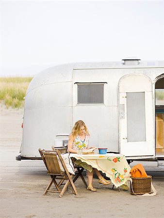 woman sitting at a table on the beach outside her airstream classic trailer Foto de stock - Sin royalties Premium, Código: 640-02952827