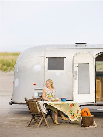 woman sitting at a table on the beach outside her airstream classic trailer Foto de stock - Sin royalties Premium, Código: 640-02952828