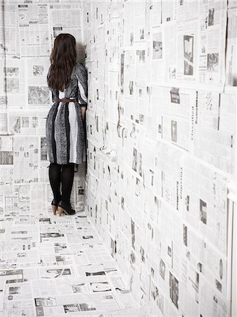 Young woman standing in corner of room covered with newspapers Stock Photo - Premium Royalty-Free, Code: 640-03256374