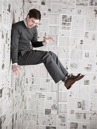 fels - Young man stuck to wall covered with newspapers, studio shot Stock Photo - Premium Royalty-Free, Code: 640-03256379