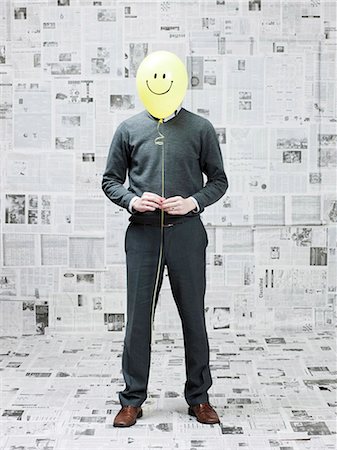 smiley - Young man covering face with smiley balloon in newspaper room Stock Photo - Premium Royalty-Free, Code: 640-03256387