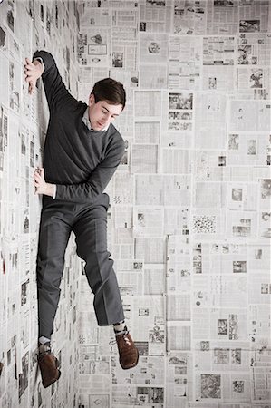 fels - Young man stuck to wall covered with newspapers, studio shot Stock Photo - Premium Royalty-Free, Code: 640-03256380