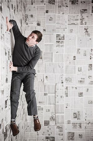 Young man stuck to wall covered with newspapers trying to escape, studio shot Foto de stock - Sin royalties Premium, Código: 640-03256381