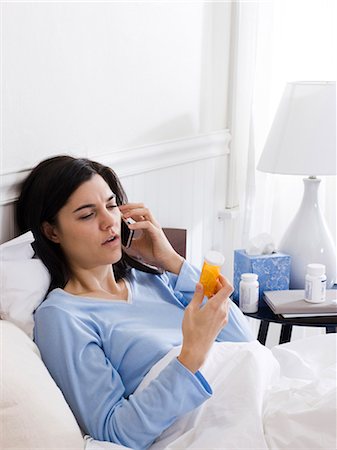 Orem, Utah, USA, young ill woman in bed looking at pill bottle and talking on the phone Stock Photo - Premium Royalty-Free, Code: 640-03256708