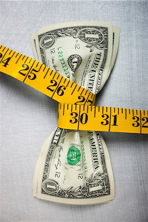 Studio shot of yellow measure tape squeezing two one dollar bills Stock Photo - Premium Royalty-Free, Code: 640-03256903