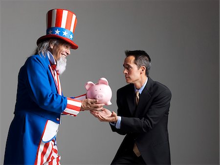 piggy bank and smiling - Man in Uncle Sam's costume giving piggybank to other man, studio shot Stock Photo - Premium Royalty-Free, Code: 640-03257654