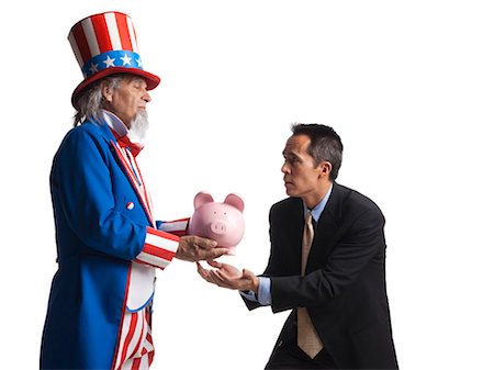 Man in Uncle Sam's costume giving piggybank to other man, studio shot Stock Photo - Premium Royalty-Free, Code: 640-03257655