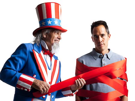 Man in Uncle Sam's costume wrapping other man with ribbon, studio shot Stock Photo - Premium Royalty-Free, Code: 640-03257650