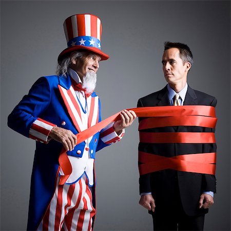 simsearch:640-03257652,k - Man in Uncle Sam's costume wrapping other man with ribbon, studio shot Stock Photo - Premium Royalty-Free, Code: 640-03257651
