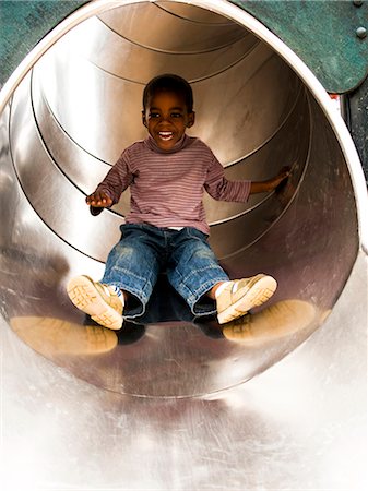 Boy sliding down playground slide stock photo