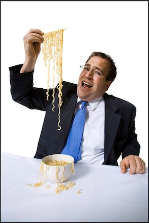 Businessman awkwardly eating noodles Stock Photo - Premium Royalty-Free, Code: 640-03265126
