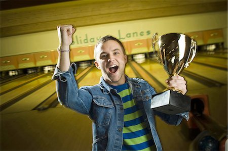 Portrait of a young man holding a bowling trophy and gesturing with his hand Stock Photo - Premium Royalty-Free, Code: 640-03265602