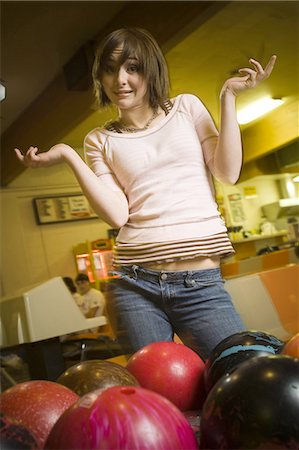 Low angle view of a teenage girl looking at bowling balls and scratching her head Stock Photo - Premium Royalty-Free, Code: 640-03265617