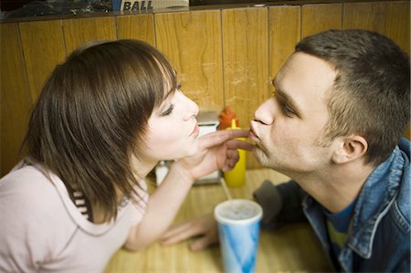 High angle view of a young man and a teenage girl sitting in a restaurant and leaning forward to kiss Foto de stock - Sin royalties Premium, Código: 640-03265621