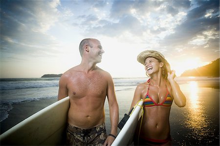 Man and woman holding a surfboard and looking at each other Stock Photo - Premium Royalty-Free, Code: 640-03265768