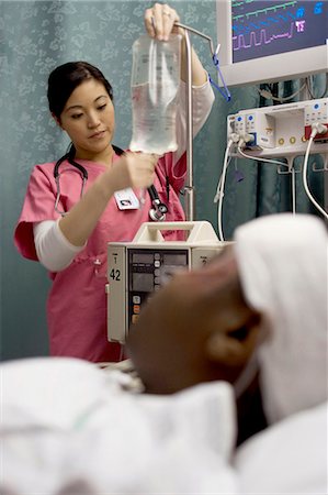 sick black patient photo bandaged in hospital bed - Nurse adjusting IV bag for patient Stock Photo - Premium Royalty-Free, Code: 640-03261828