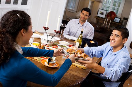 sitting to eat at dinner table - Boy passing chicken to man at table Stock Photo - Premium Royalty-Free, Code: 640-03262684