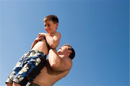 simsearch:640-02773934,k - Man holding boy up with blue sky Foto de stock - Royalty Free Premium, Número: 640-03262821