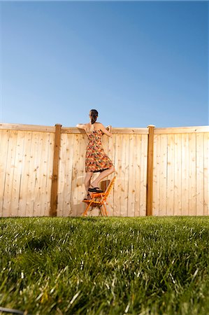 Woman standing on chair peeping over fence Stock Photo - Premium Royalty-Free, Code: 640-03262835