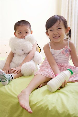 Boy and girl playing with doll and a bottle of milk in bed Stock Photo - Premium Royalty-Free, Code: 642-01734331