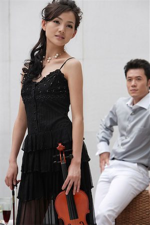 Jeune femme tenant un violon avec un homme en arrière-plan Photographie de stock - Premium Libres de Droits, Code: 642-01734463