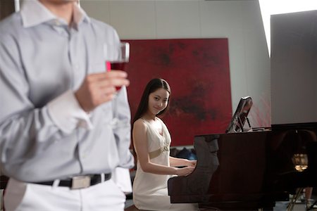 Woman playing piano with man holding wineglass in the foreground Stock Photo - Premium Royalty-Free, Code: 642-01734508