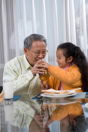 Granddaughter feeding juice to grandfather and smiling Stock Photo - Premium Royalty-Free, Code: 642-01735003