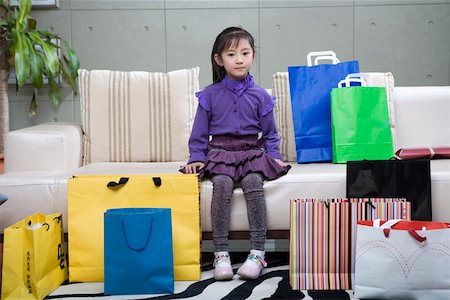 Girl sitting on sofa by shopping bag, smiling, portrait Stock Photo - Premium Royalty-Free, Code: 642-01735140