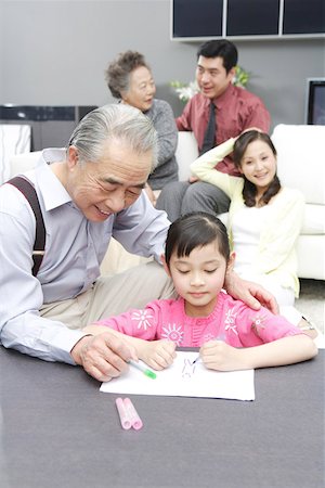 Girl drawing with grandfather while family sitting behind Stock Photo - Premium Royalty-Free, Code: 642-01735314
