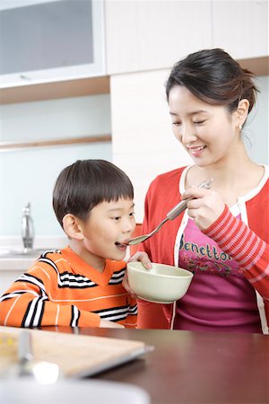 feeding asian family - Mother feeding boy in kitchen Stock Photo - Premium Royalty-Free, Code: 642-01735373