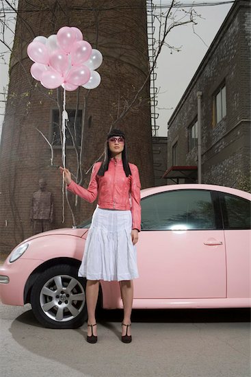 Young woman holding balloons in front of car Stock Photo - Premium Royalty-Free, Image code: 642-01735402