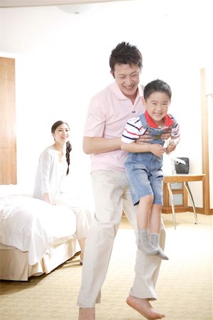 Young man holding a son while woman sitting behind on bed, smiling Stock Photo - Premium Royalty-Free, Code: 642-01735614