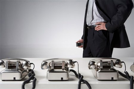 Midsection of a businessman standing by desk with telephones Stock Photo - Premium Royalty-Free, Code: 642-01736414