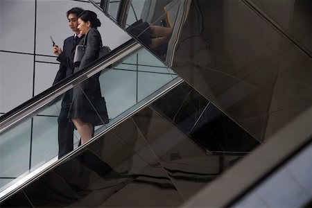 Businessman and businesswoman using mobile phone on escalators Stock Photo - Premium Royalty-Free, Code: 642-01736554