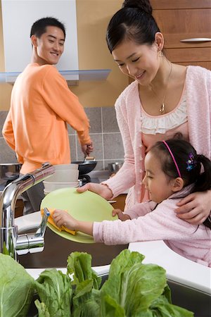 family cleaning - Portrait of a mother and daughter cleaning plate while man cooking food in background Stock Photo - Premium Royalty-Free, Code: 642-01736644