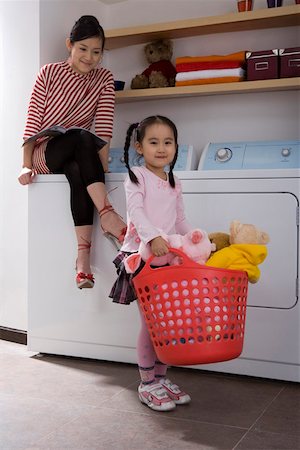 Young woman sitting on washing machine while girl holding basket and smiling Stock Photo - Premium Royalty-Free, Code: 642-01736665