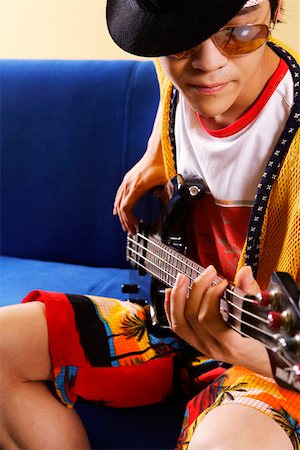 simsearch:640-03256775,k - Fashionable young man playing guitar in blue sofa Fotografie stock - Premium Royalty-Free, Codice: 642-01736866