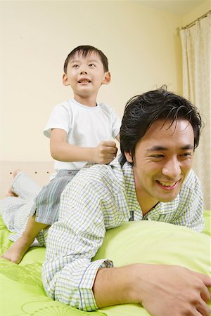 Son riding on father on bed Stock Photo - Premium Royalty-Free, Code: 642-01736984