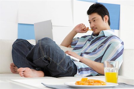 Young man playing laptop in sofa behind food and drink Stock Photo - Premium Royalty-Free, Code: 642-01737034