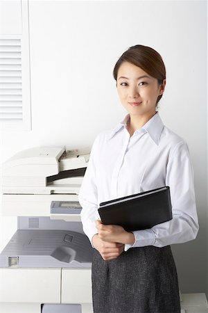 Young woman holding a file behind copy machine Stock Photo - Premium Royalty-Free, Code: 642-01737079