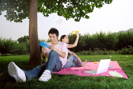 Young couple sitting under tree and holding paper airplane Stock Photo - Premium Royalty-Free, Code: 642-01737171