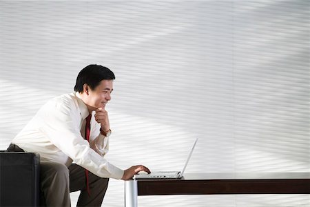 executive office profile - Businessman using laptop in office, smiling Stock Photo - Premium Royalty-Free, Code: 642-01737461