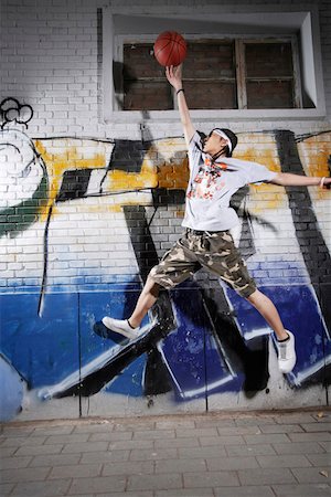 Young man playing basketball in front of graffiti Stock Photo - Premium Royalty-Free, Code: 642-01733359