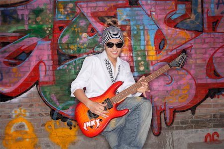 Young man wearing sunglasses playing guitar in front of a wall with graffiti Stock Photo - Premium Royalty-Free, Code: 642-01733405