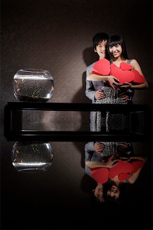 Young couple holding heart- shapped gift boxes beside a fishbowl in the darkness Stock Photo - Premium Royalty-Free, Code: 642-01733735