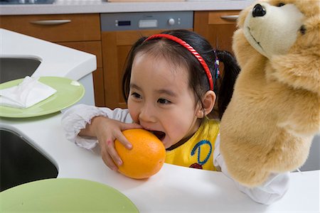 a girl in the kitchen eating orange Stock Photo - Premium Royalty-Free, Code: 642-02006705