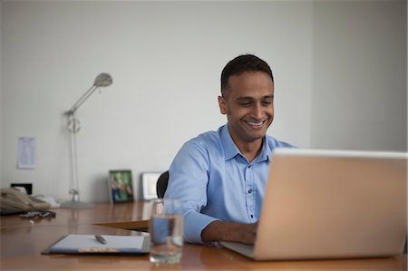 person sitting at desk picture - Singapore, Smiling businessman working at laptop in office Stock Photo - Premium Royalty-Free, Code: 655-08356913