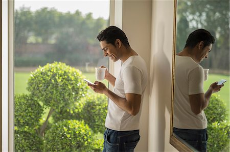 simsearch:655-08357168,k - India, Man at window using mobile phone and holding coffee cup Photographie de stock - Premium Libres de Droits, Code: 655-08356965