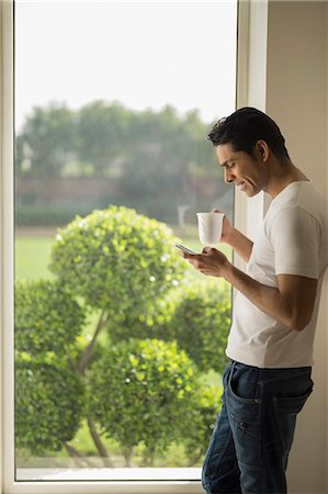 simsearch:655-08357168,k - India, Man at window holding coffee cup and mobile phone Photographie de stock - Premium Libres de Droits, Code: 655-08356962